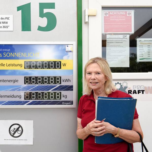 Eine Frau steht neben dem Zähler einer Photovoltaikanlage.