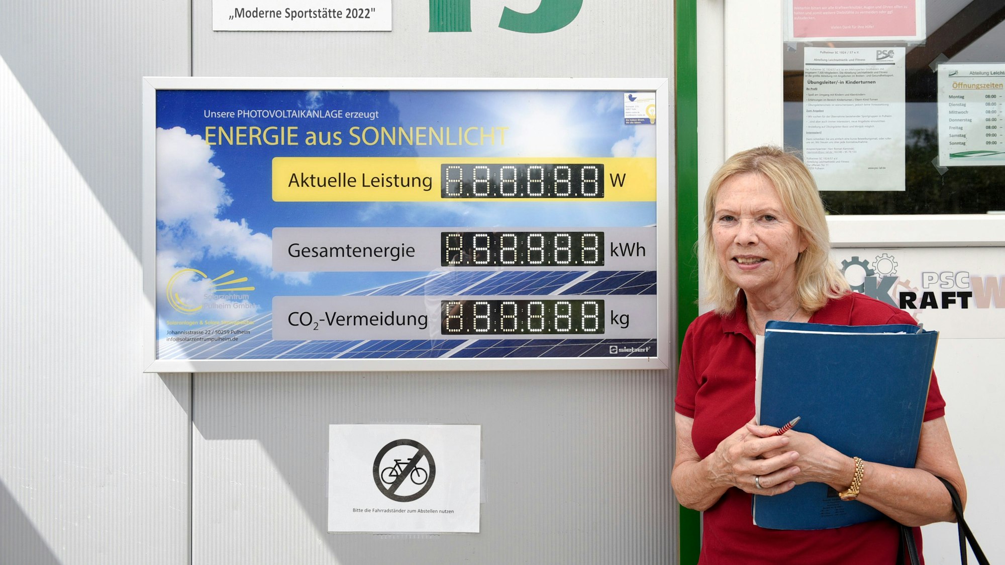 Eine Frau steht neben dem Zähler einer Photovoltaikanlage.