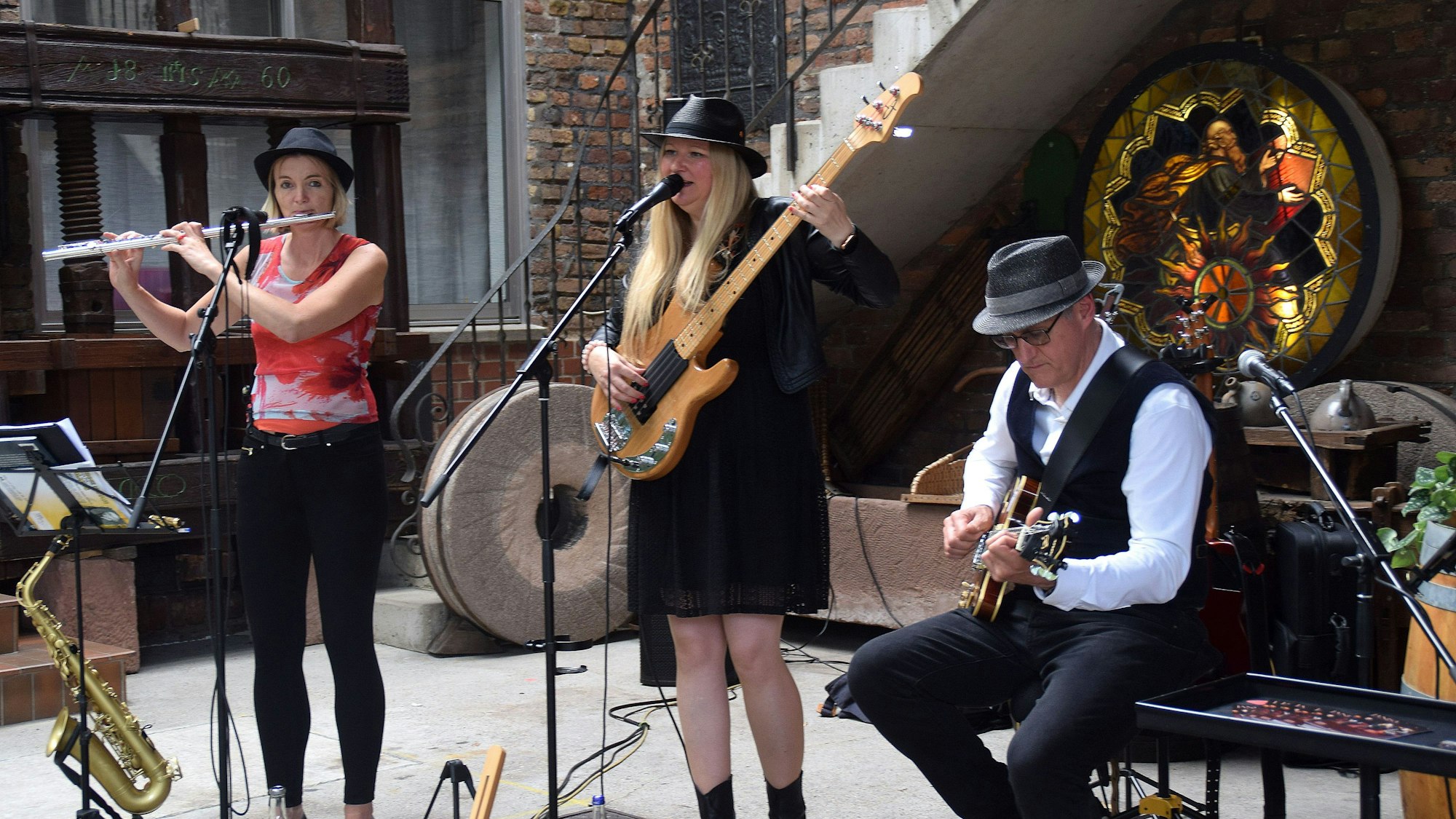 Zwei Frauen und ein Mann machen mit Instrumenten Musik. Eine Frau singt in ein Mikrofon.
