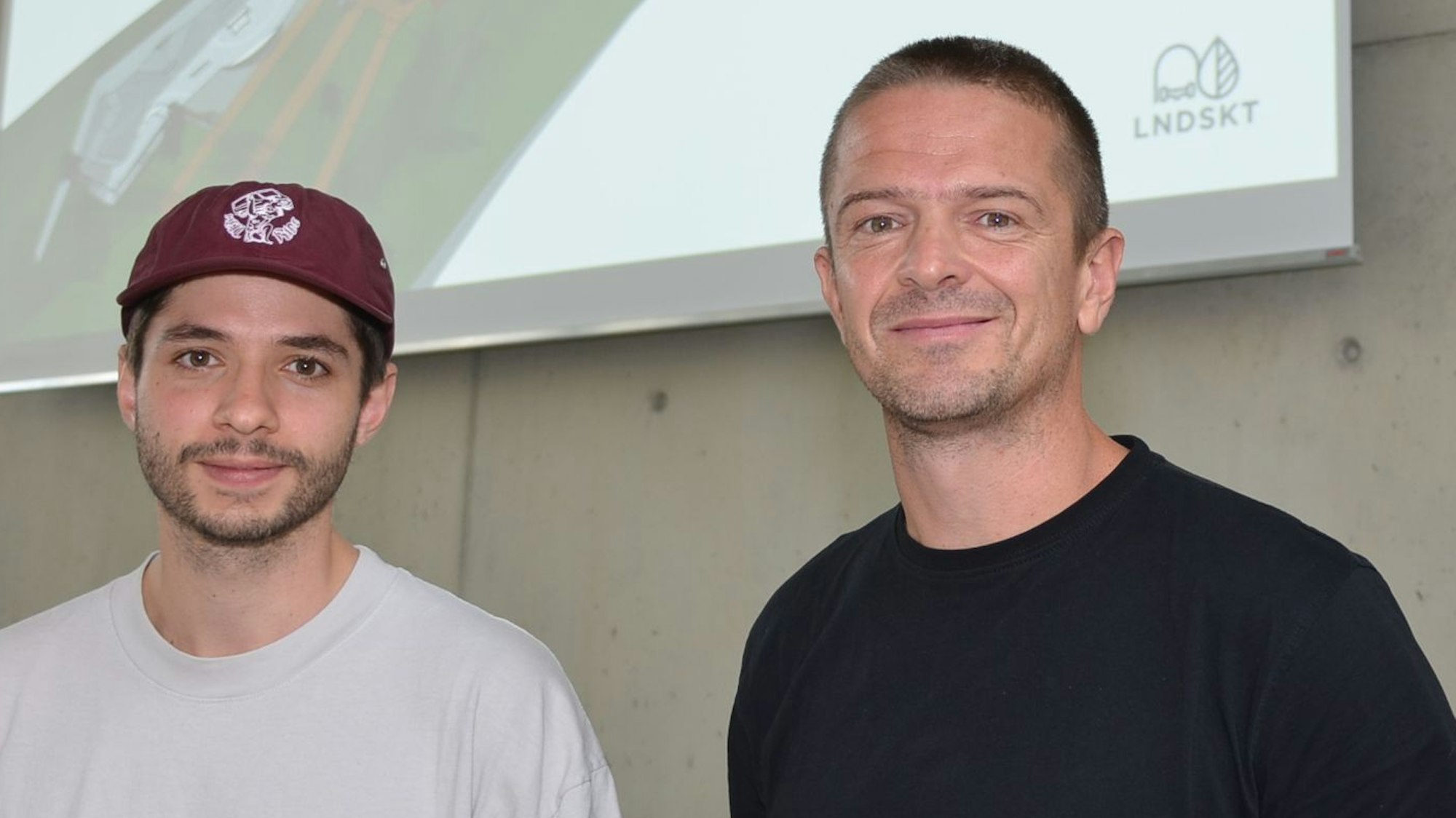 Daniel Schreitmüller (links) und Tobias Hunger von der Landskate GmbH in Köln planen den Rollsport an der Klus in der Ortschaft Niederhof. Jetzt haben sie in Waldbröls Bürgerdorf am Alsberg ihre Pläne in 3D vorgestellt. Sie stehen vor einer Leinwand.