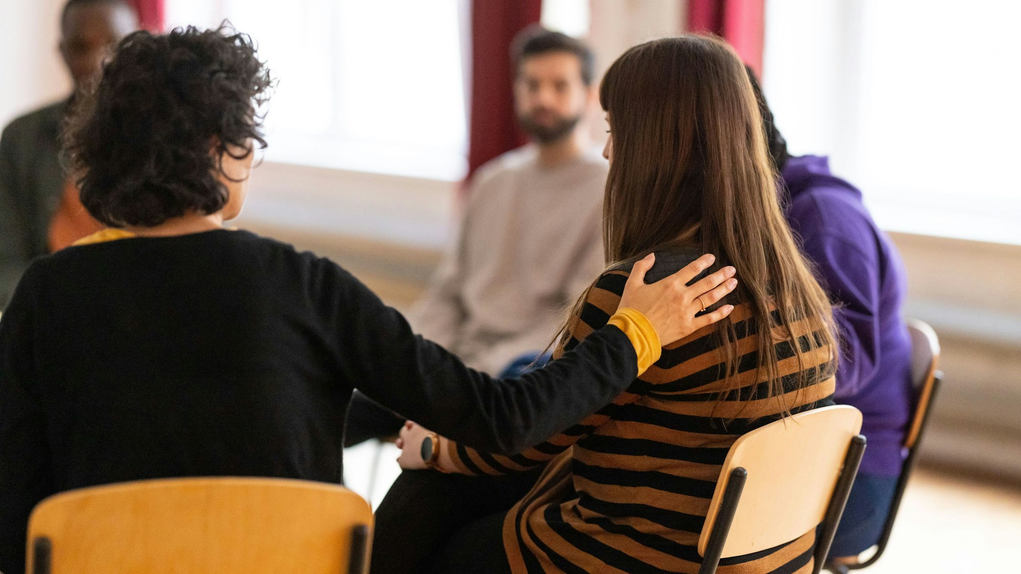 Eine Frau legt einer anderen Frau in einem Stuhlkreis die Hand auf die Schulter.