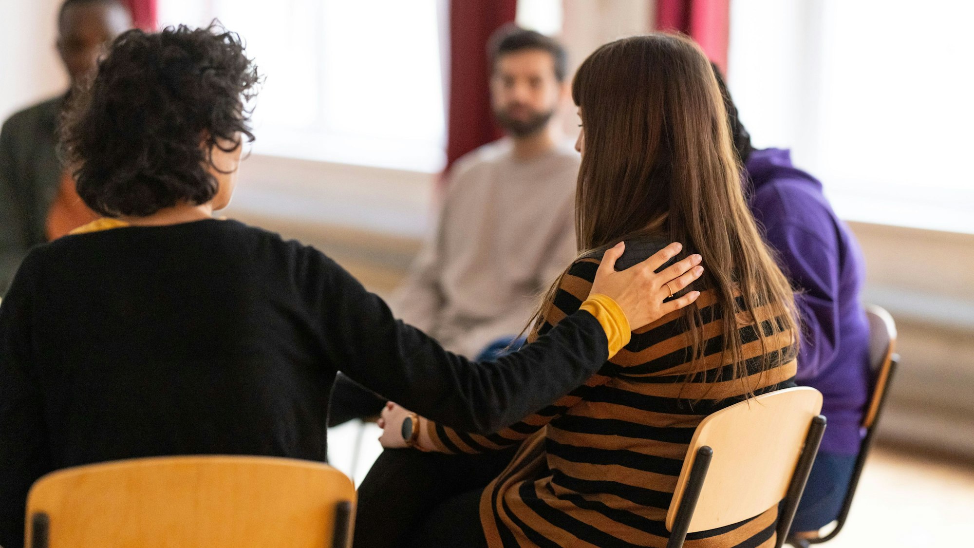 Eine Frau legt einer anderen Frau in einem Stuhlkreis die Hand auf die Schulter.