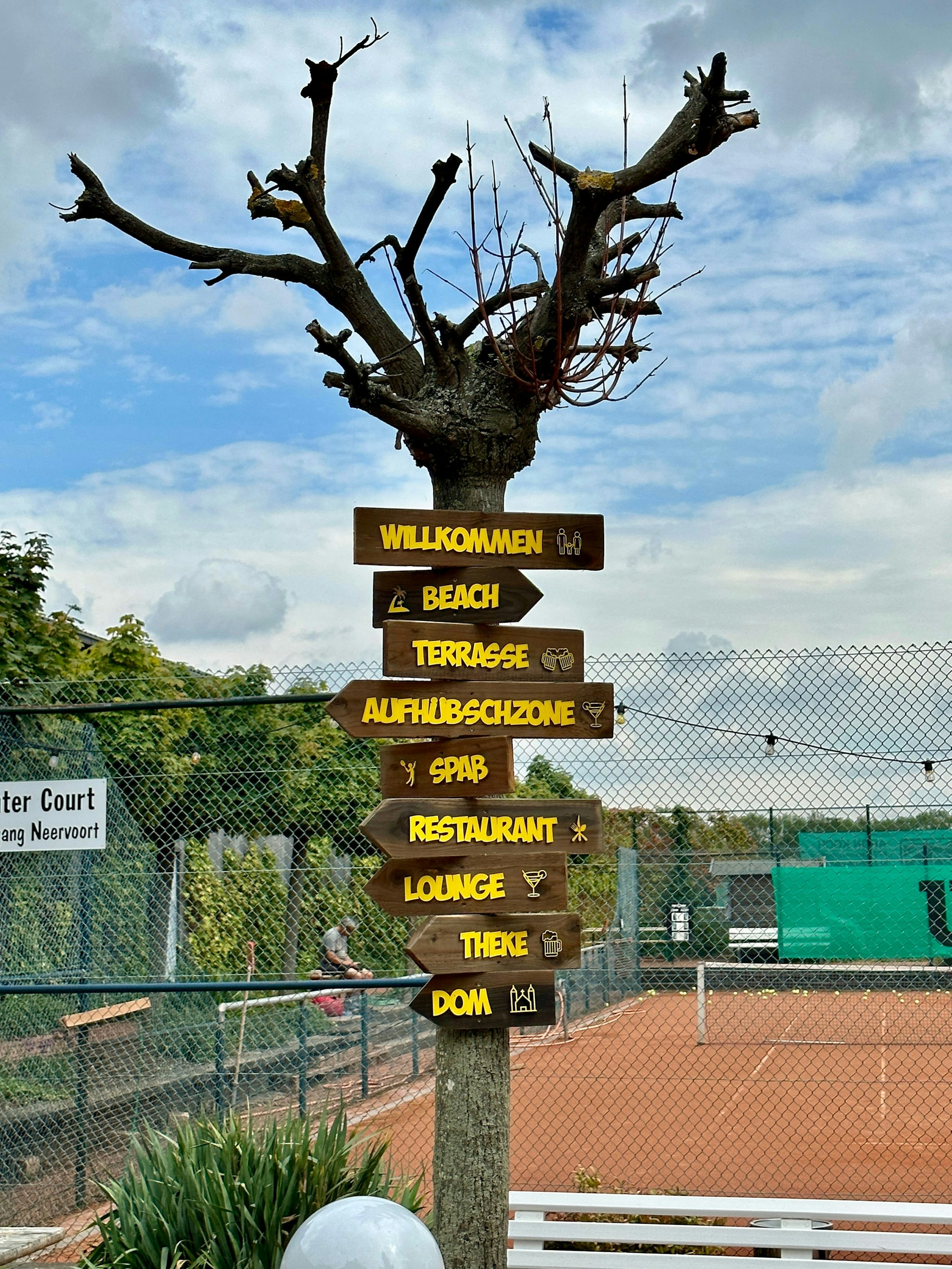 Holzschilder sind an eine Holzlatte genagelt. Sie weisen zu Lounge, Theke, Restaurant oder Dom.