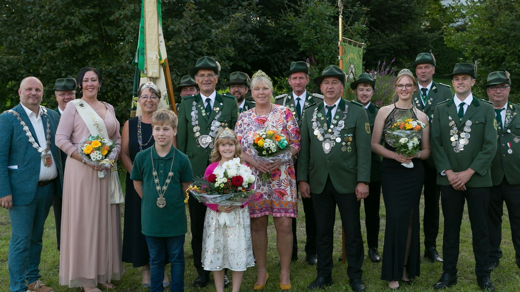 Zu sehen sind festlich gekleidete Frauen und Männer auf einer Wiese.