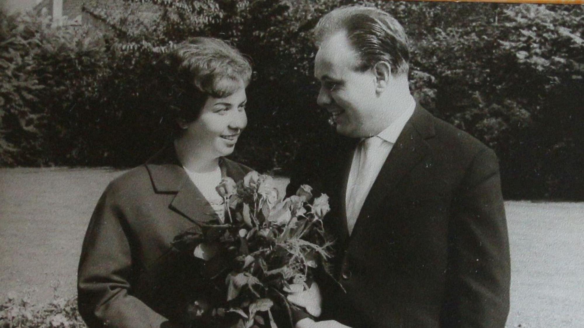 Eine Frau mit Blumenstrauß und ein Mann stehen nebeneinander und lächeln sich an.