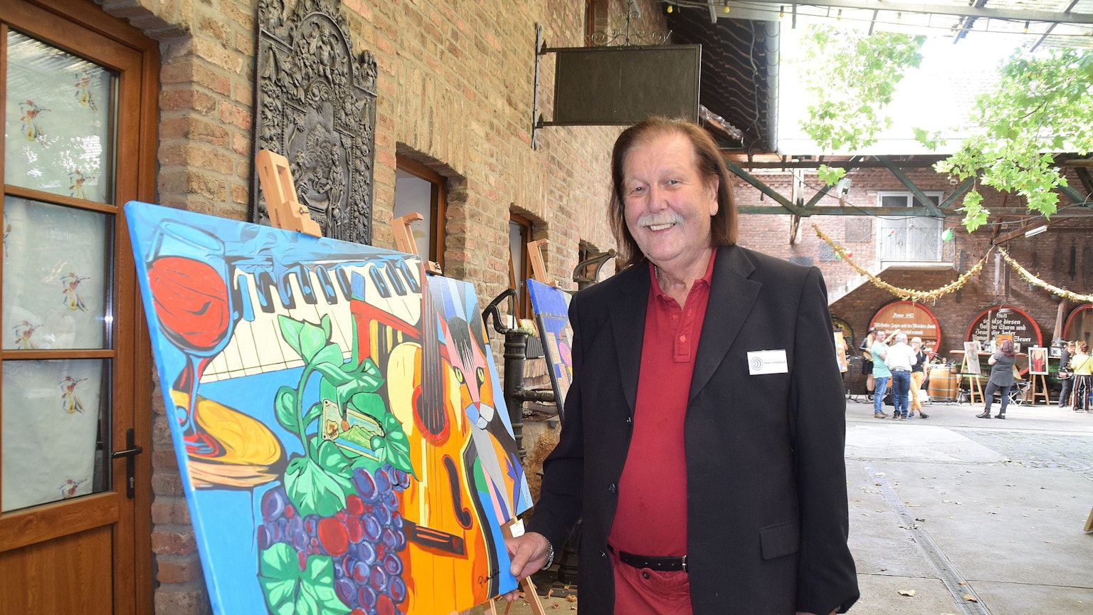 Ein Mann steht neben einer Staffelei, auf der ein buntes Bild steht.