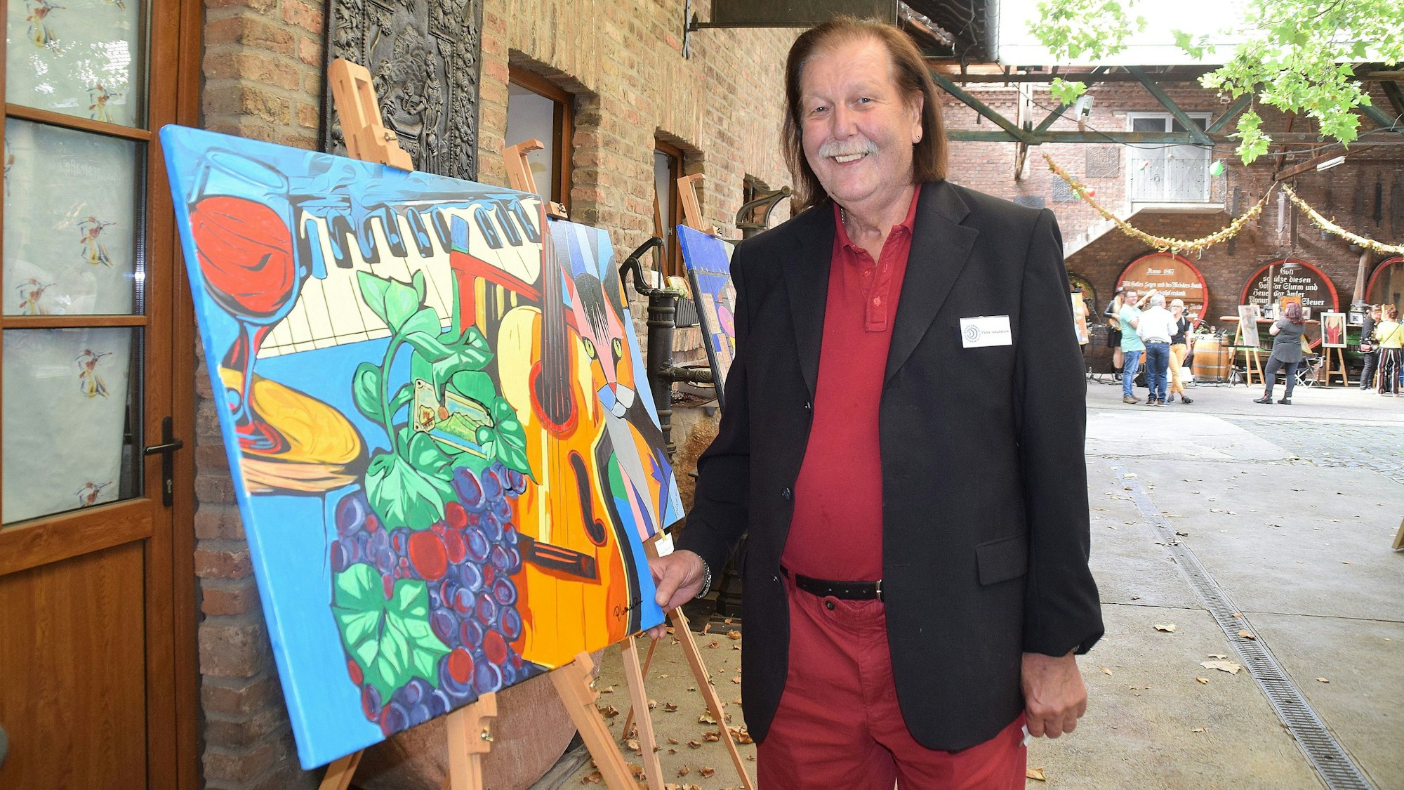 Ein Mann steht neben einer Staffelei, auf der ein buntes Bild steht.