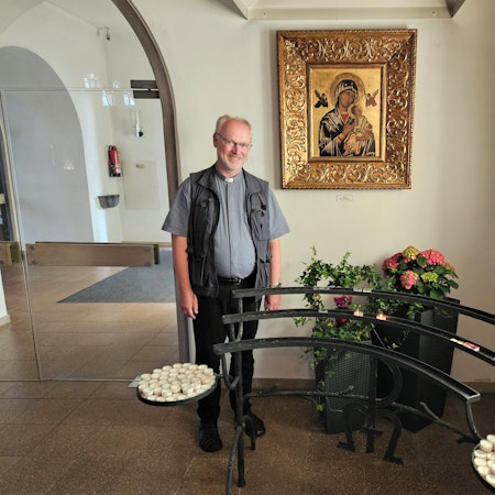 Pfarrer Klemens Gößmann steht vor einem Marienbildnis mit Blumen und Kerzen.