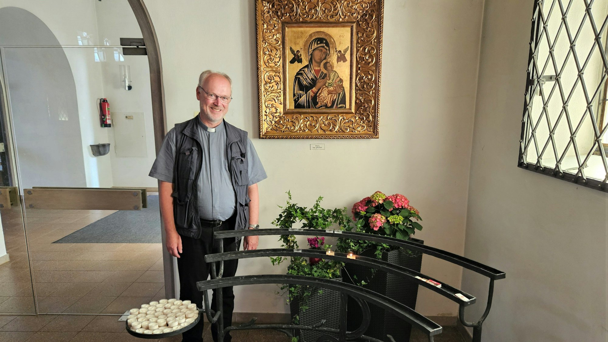 Pfarrer Klemens Gößmann steht vor einem Marienbildnis mit Blumen und Kerzen.