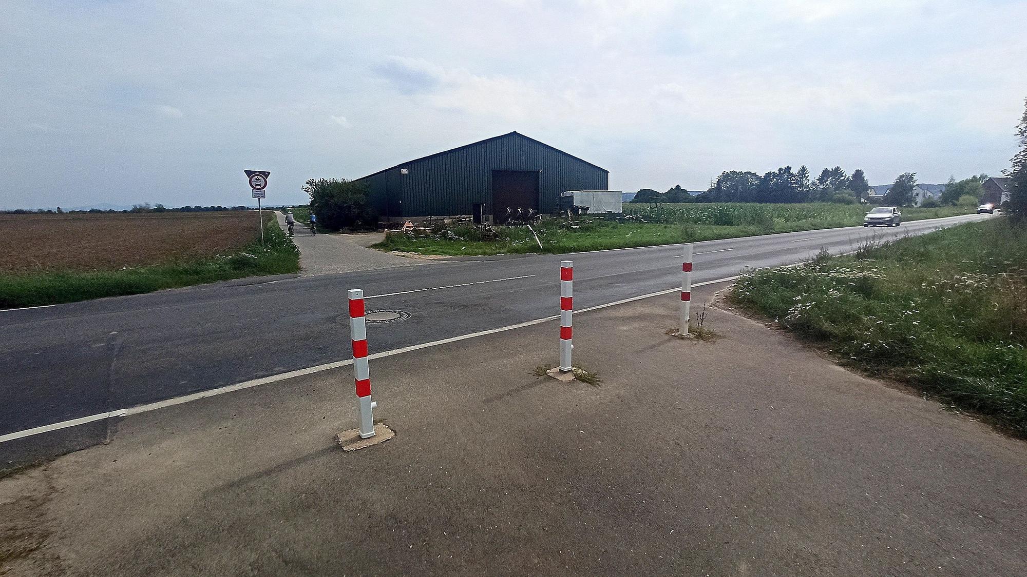 Eine Landstraße und ein Weg, der durch Begrenzungspoller abgesperrt ist.
