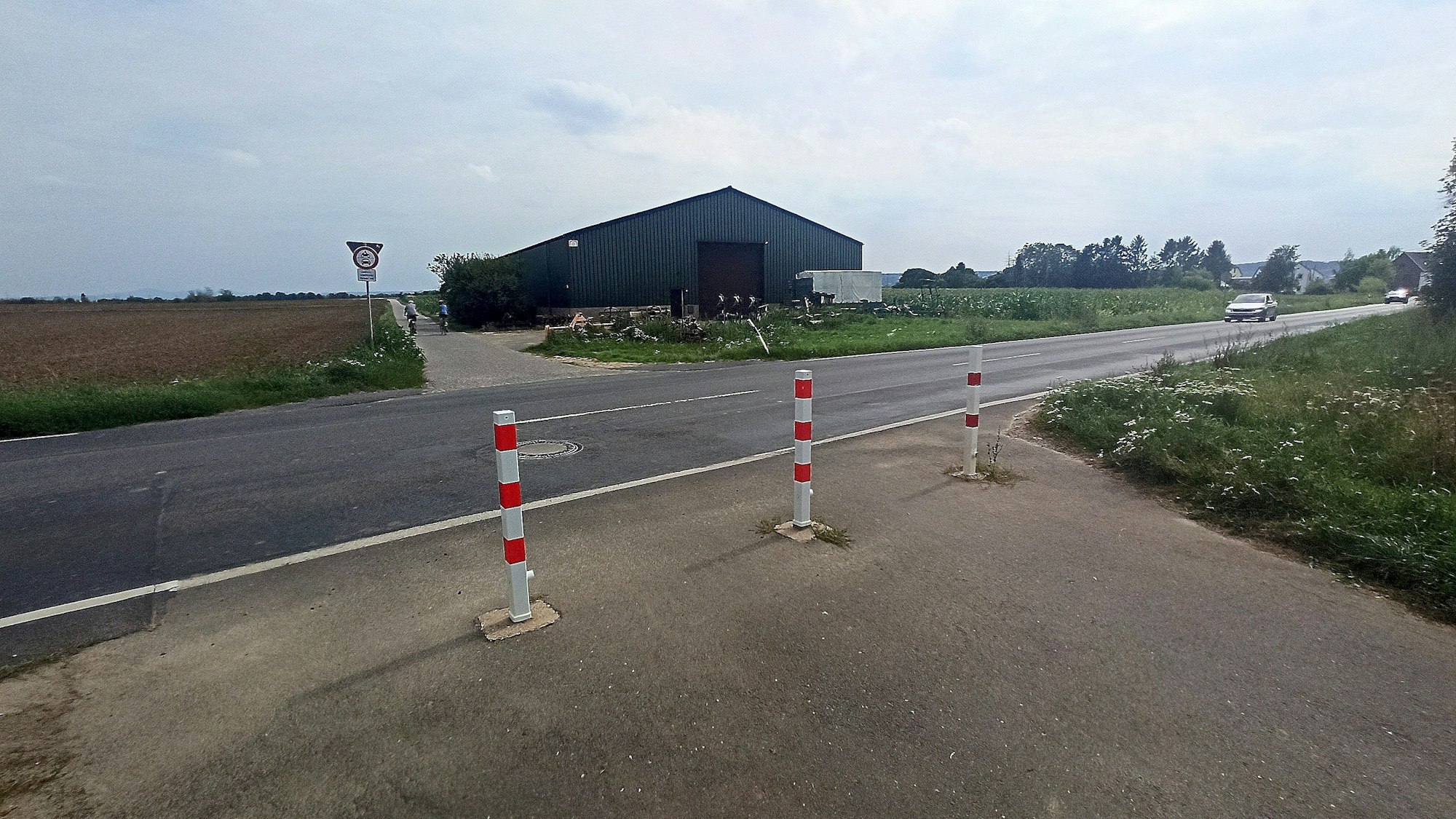 Eine Landstraße und ein Weg, der durch Begrenzungspoller abgesperrt ist.