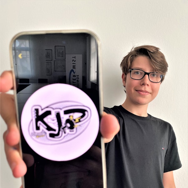 Simon Krämer, Vorsitzender des Kinder- und Jugendparlaments, hält sein Smartphone in die Kamera. Darauf zu sehen: das Logo des Kinder- und Jugendparlaments (KJP).