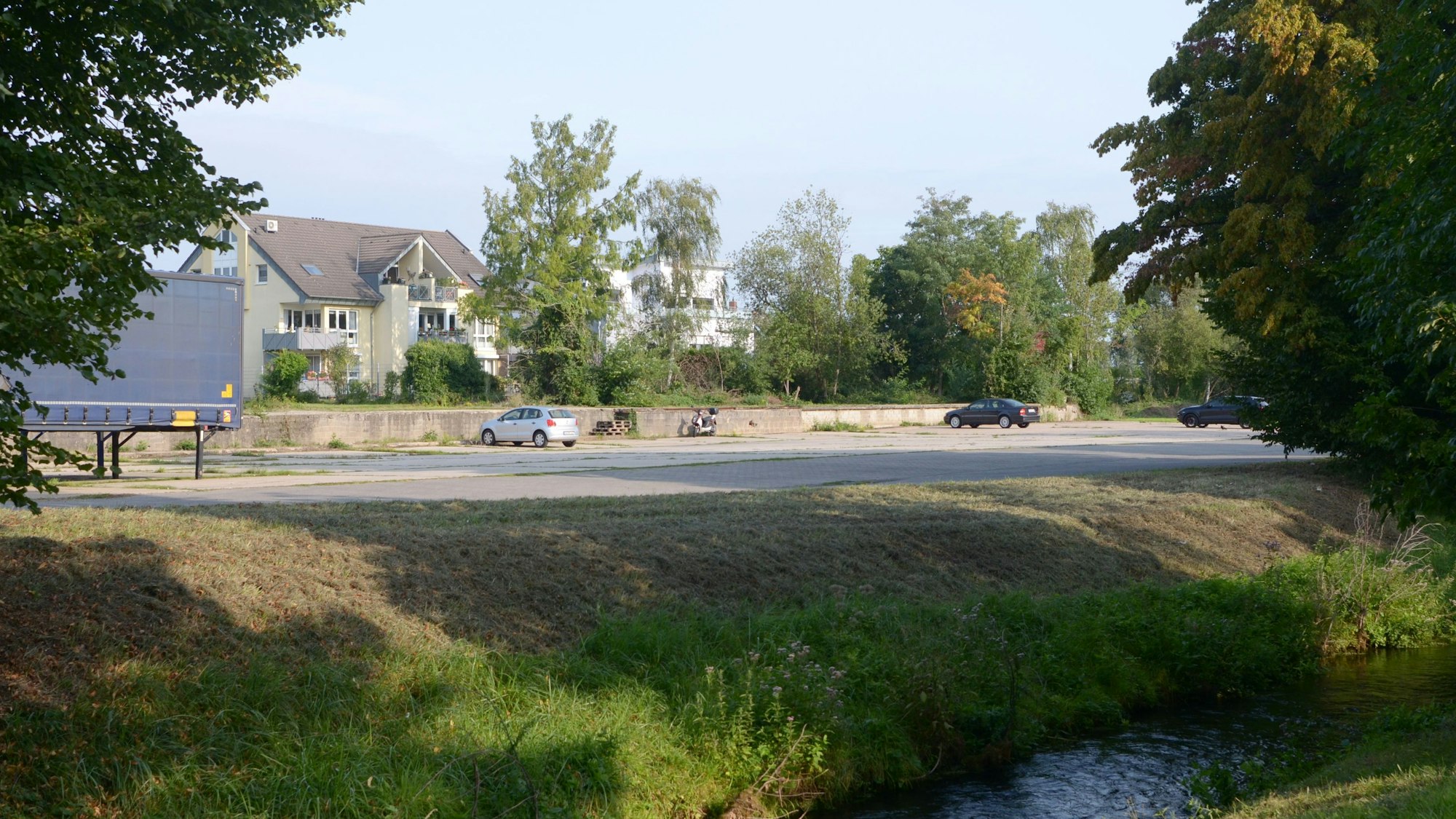 Auf einem Grundstück am Veybach in Euskirchen stehen mehrere Autos. Der größte Teil des Areals ist ungenutzt. Dort sollen Wohnhäuser entstehen.