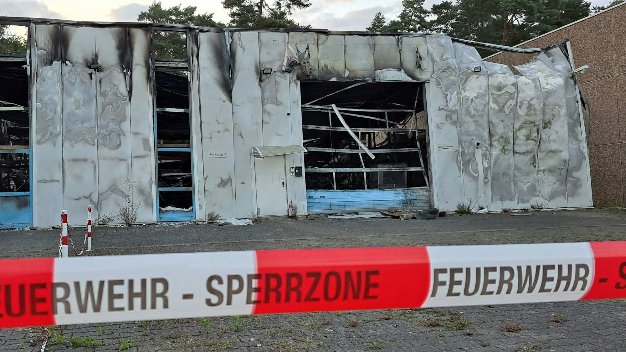Eine total ausgebrannte Halle ist mit rot-weißem Flatterband der Feuerwehr abgesperrt.
