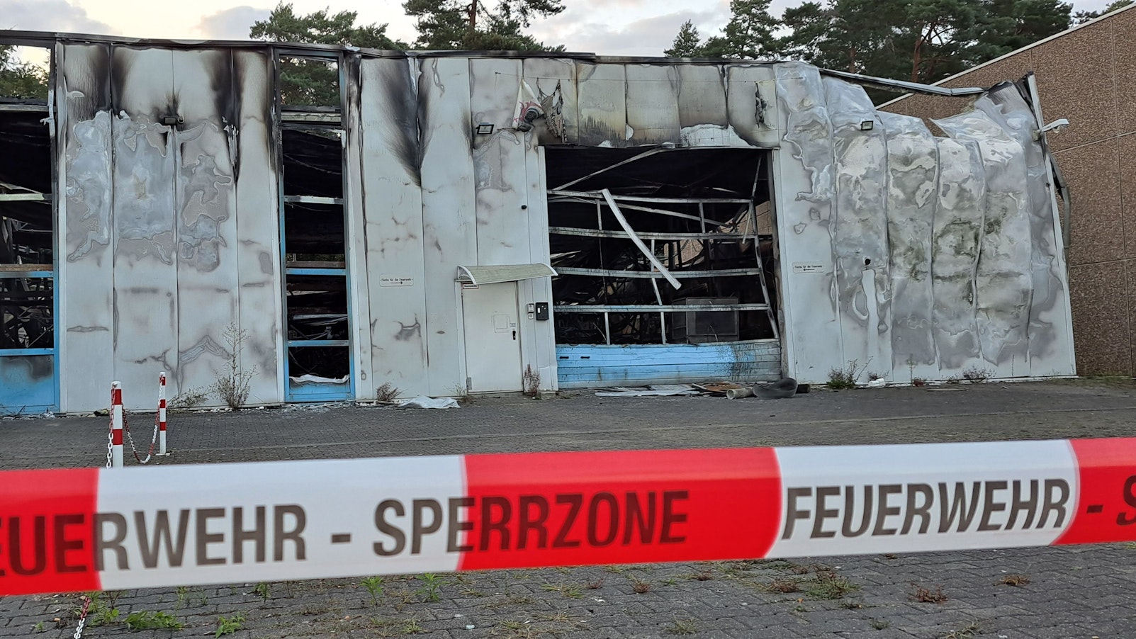 Eine total ausgebrannte Halle ist mit rot-weißem Flatterband der Feuerwehr abgesperrt.