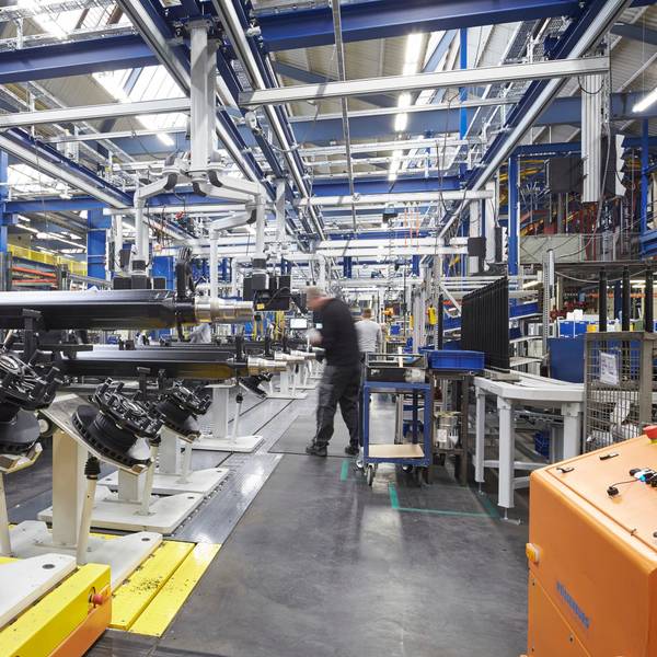Man sieht Bestandteile einer LKW-Achse und einen Arbeiter in einer großen Fabrikhalle.