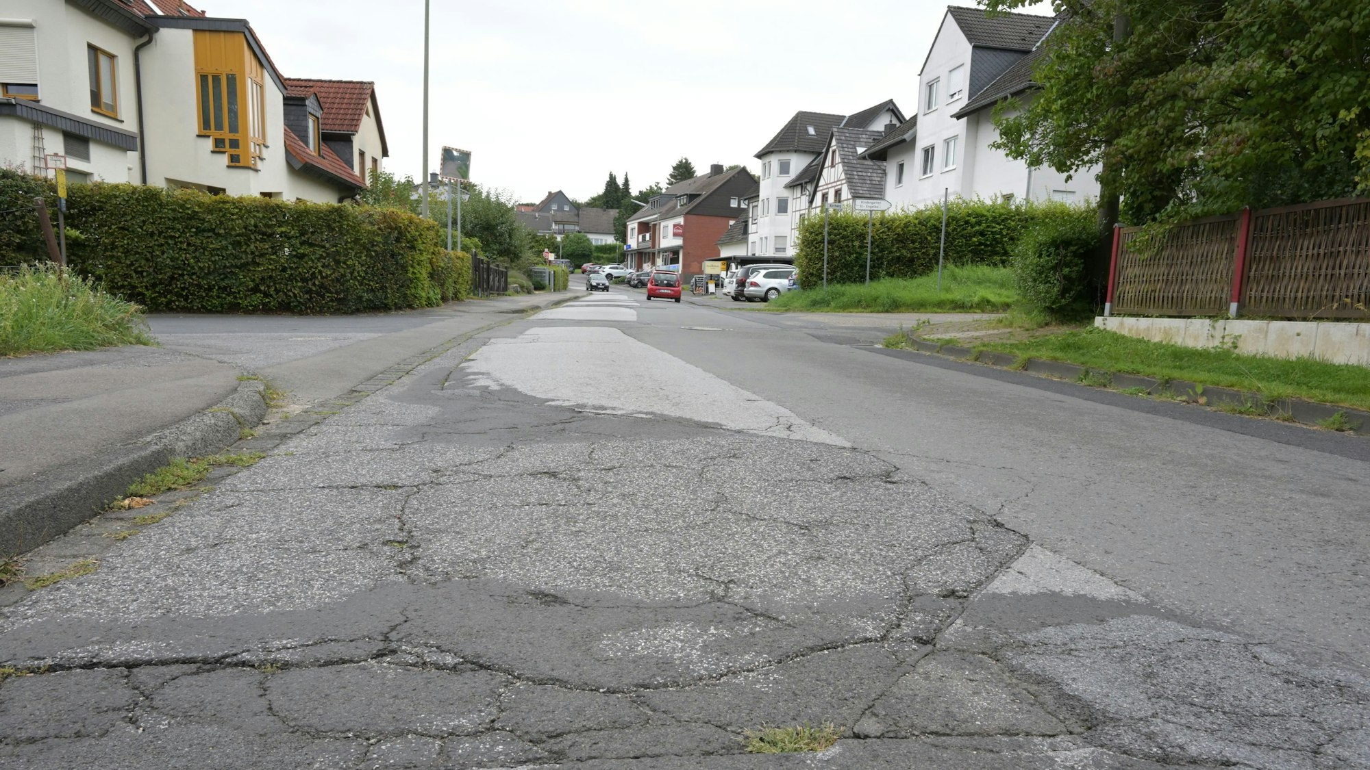Eine Straße, rechts und links bebaut, mit vielen Schäden in der Asphaltsdecke.
