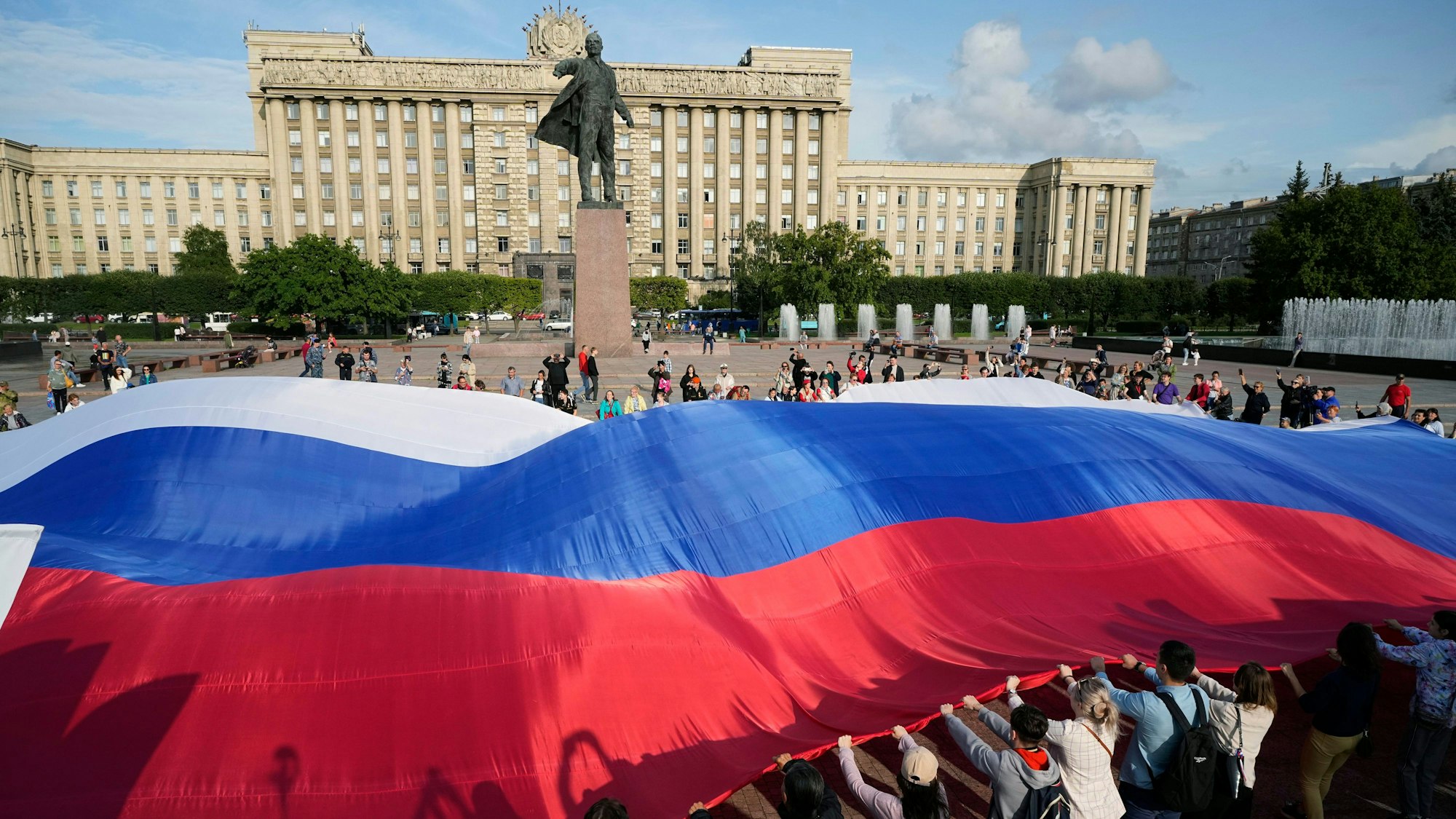 Freiwillige halten eine riesige russische Nationalflagge neben einer Statue des Gründers der Sowjetunion, Wladimir Lenin, während der Feierlichkeiten zum Tag der russischen Nationalflagge in St. Petersburg, Russland.