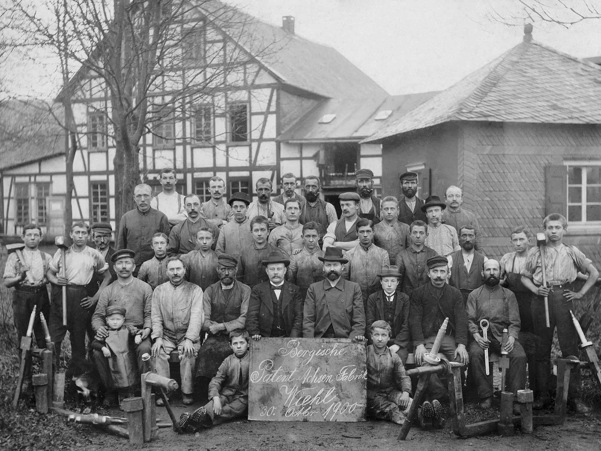 Die beiden Unternehmensgründer und ihre Arbeiter haben sich zum Gruppenbild vor einem Fachwerkgebäude formiert.