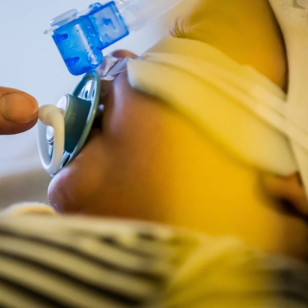 Ein Vater betreut seinen kleinen Sohn, der mit einem Atemwegsinfekt auf der Intensivstation einer Kinderklinik liegt und non-invasiv beatmet wird.