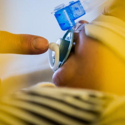 Ein Vater betreut seinen kleinen Sohn, der mit einem Atemwegsinfekt auf der Intensivstation einer Kinderklinik liegt und non-invasiv beatmet wird.