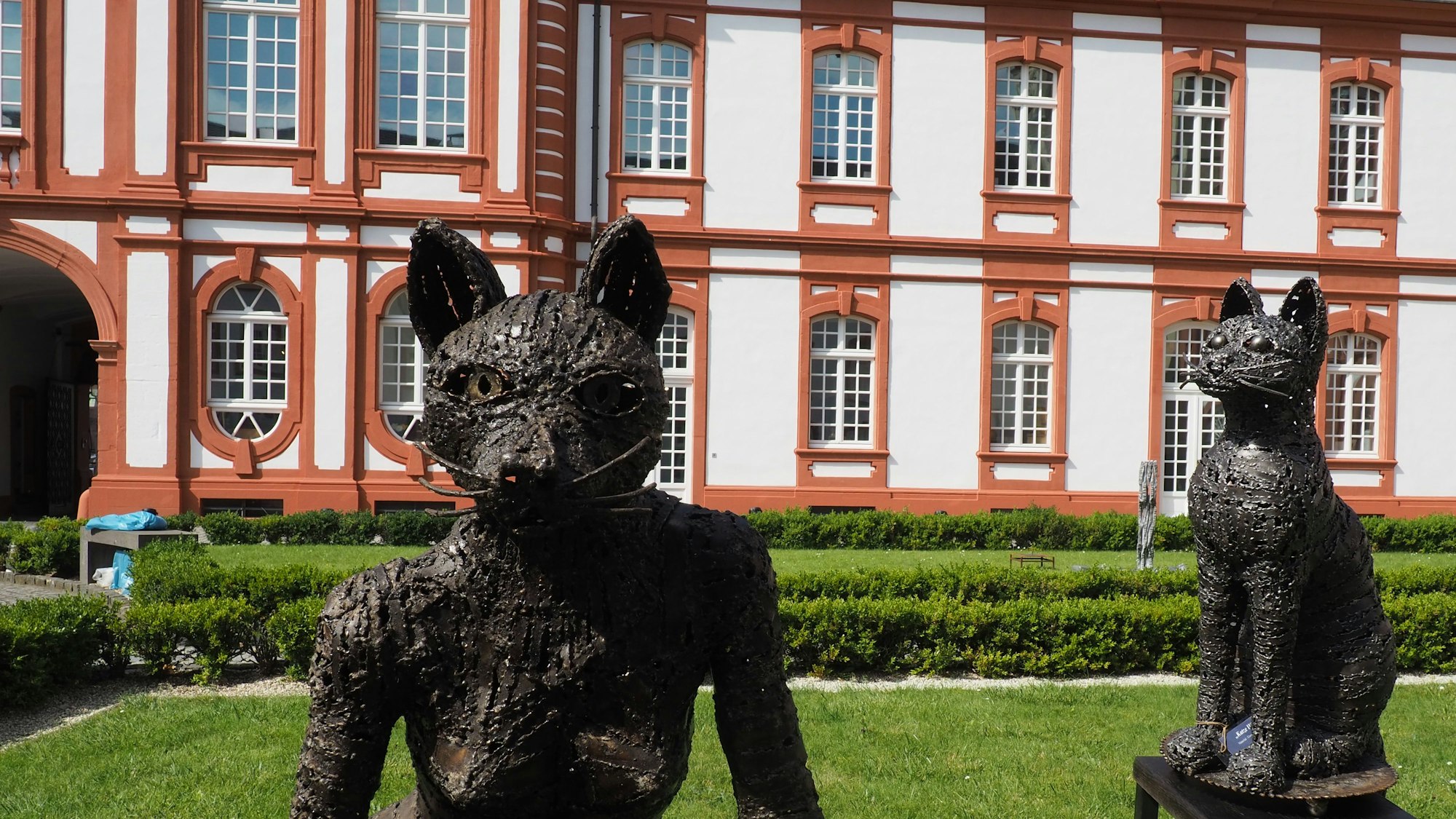 Zwei große Katzenfiguren stehen vor einer historischen Fassade.