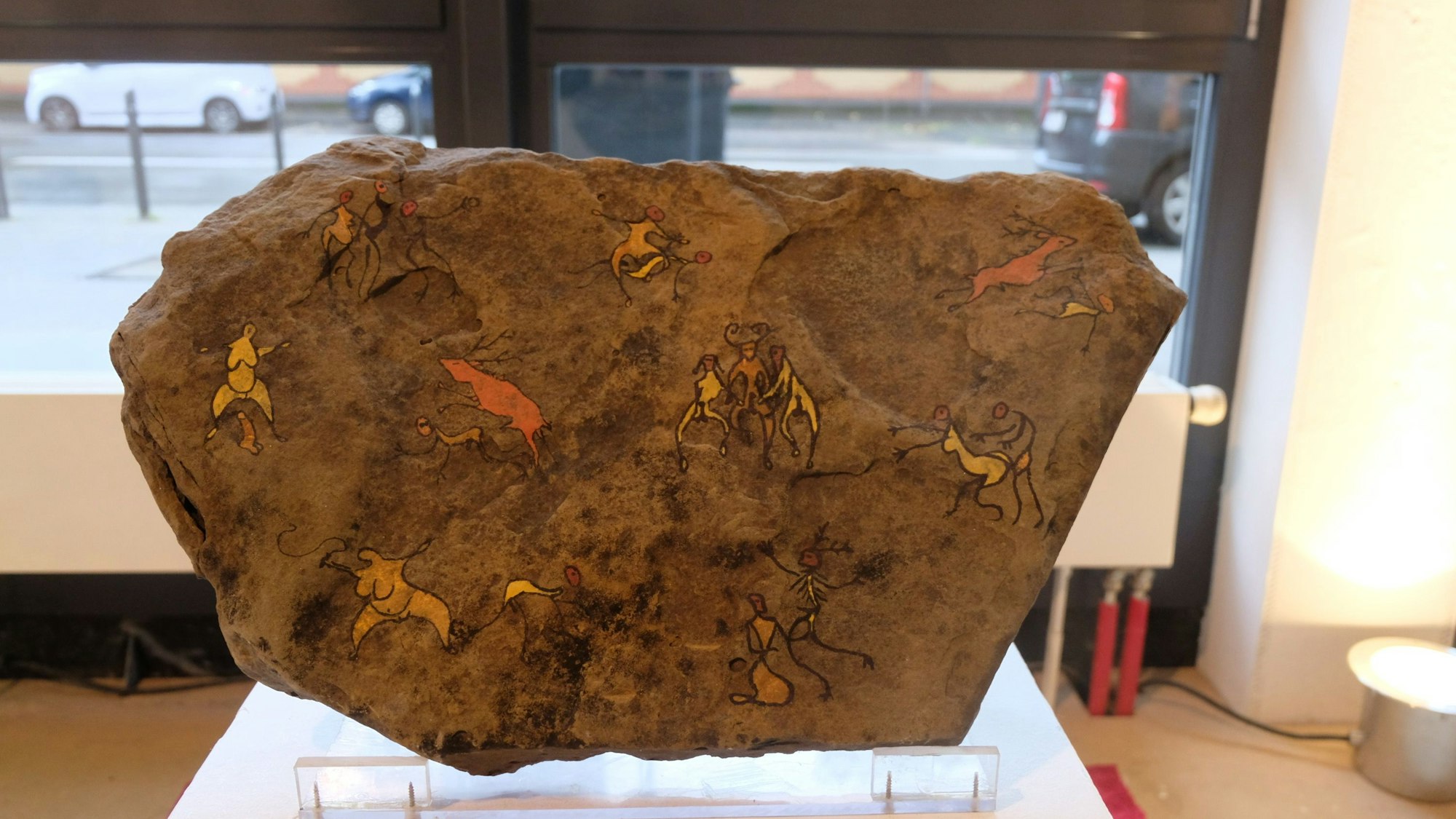 Ein großer flacher Stein ist im Stile der Höhlenmalerei mit erotischen Miniaturen bemalt.