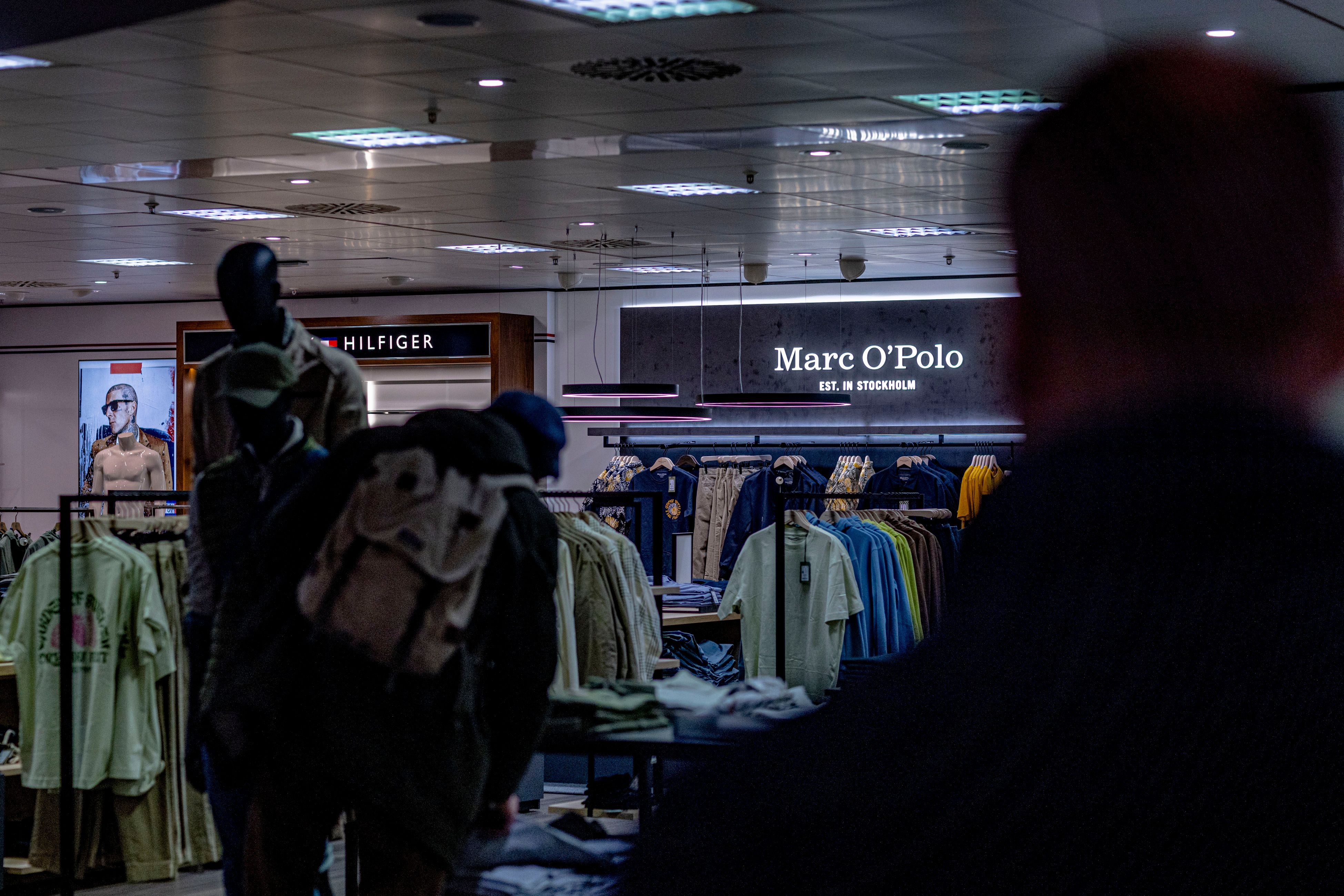 Man sieht das Innere eines Ladens, in dem eine Person mit einem Rucksack die Ware begutachtet.