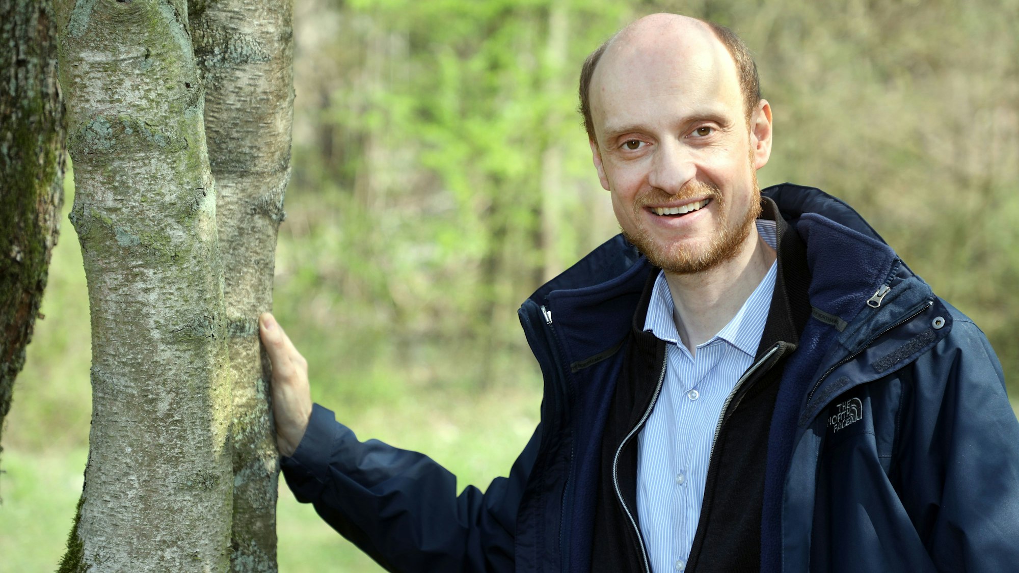 Der Biologe Dr. Bernd Freymann steht neben einem Baum und legt eine Hand auf den Stamm.