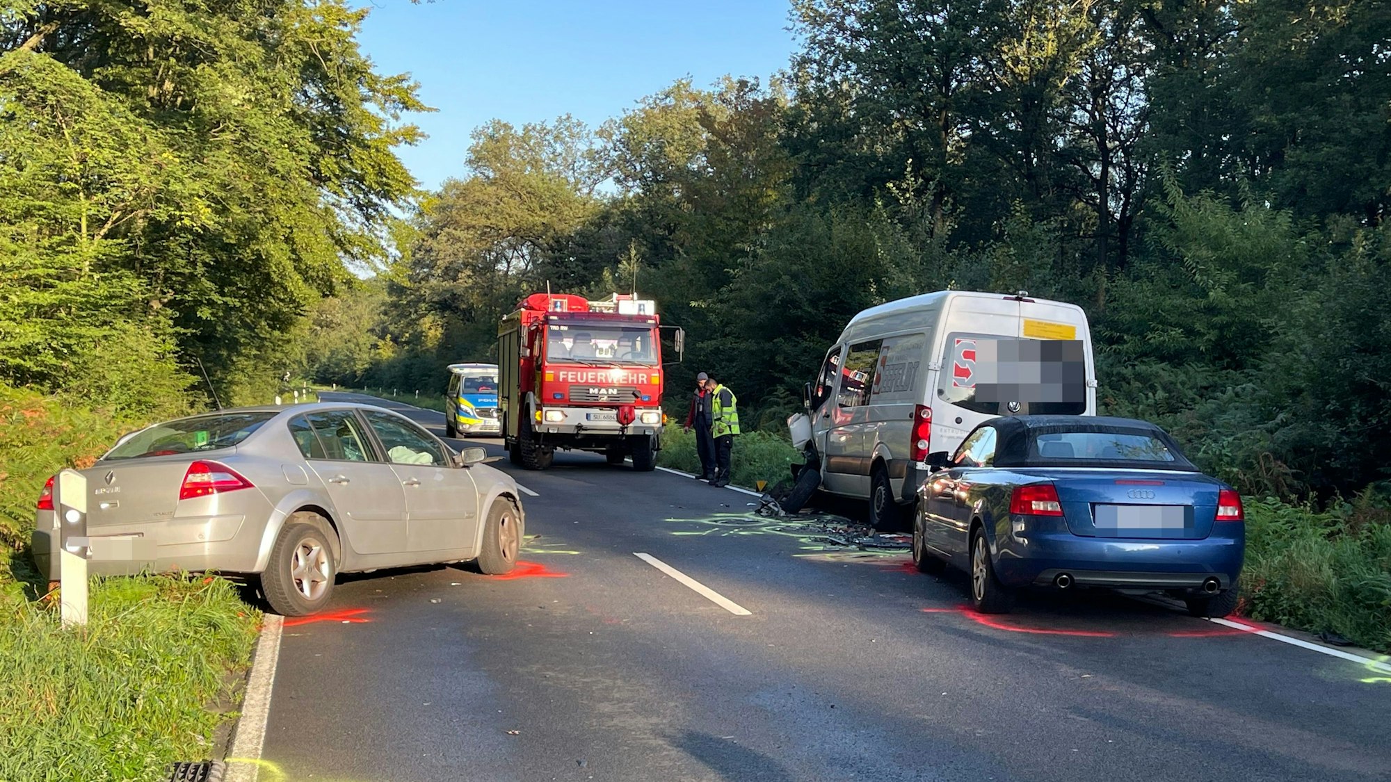 Die drei Unfallfahrzeuge stehen auf der mit Sprühfarbe markierten Straße, Fahrzeuge der Polizei und der Feuerwehr stehen dahinter.