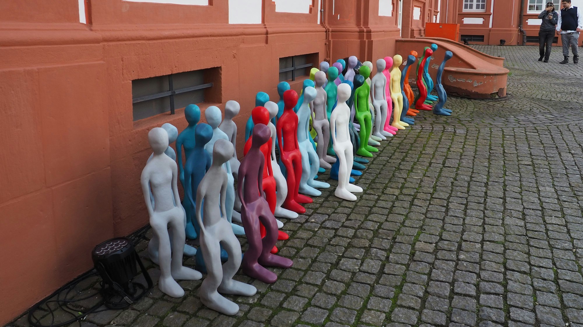 Vor einem Gebäude steht eine Reihe halbhoher, bunter Figuren.