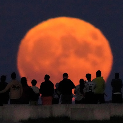 Der Vollmond erhebt sich über dem Lake Michigan, während Zuschauer vom Strand der 31st Street in Chicago aus zusehen.