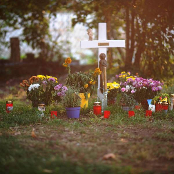 Das Bild zeigt ein weißes Holzkreuz, Blumen und Kerzen. Sie erinnern an den Tod eines Wohnungslosen.