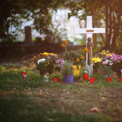 Das Bild zeigt ein weißes Holzkreuz, Blumen und Kerzen. Sie erinnern an den Tod eines Wohnungslosen.
