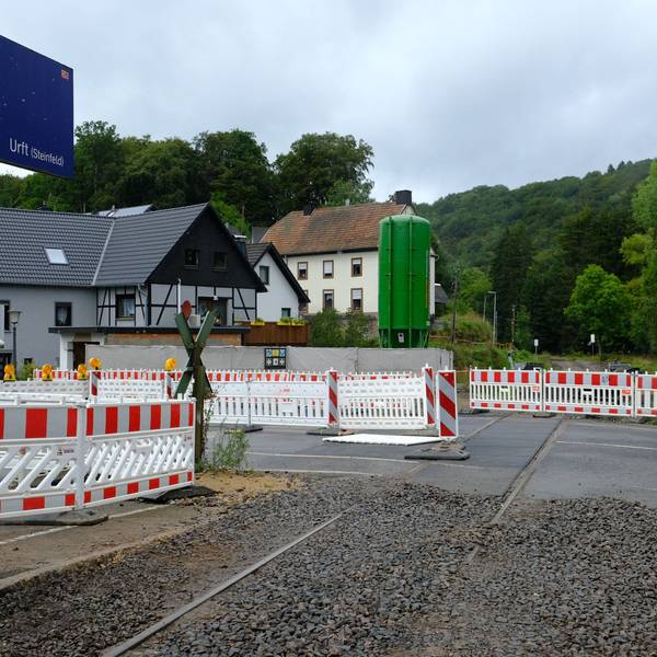 An der Baustelle des Bahnübergangs in Urft stehen Absperrungen, ein Auto fährt vorüber.