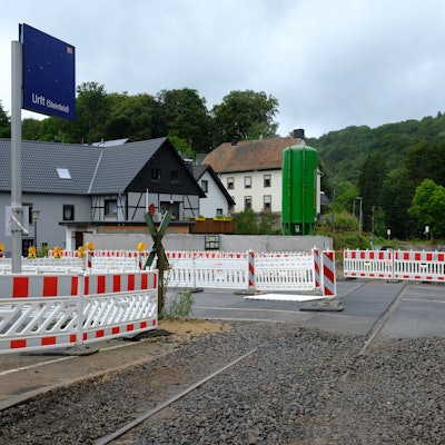 An der Baustelle des Bahnübergangs in Urft stehen Absperrungen, ein Auto fährt vorüber.