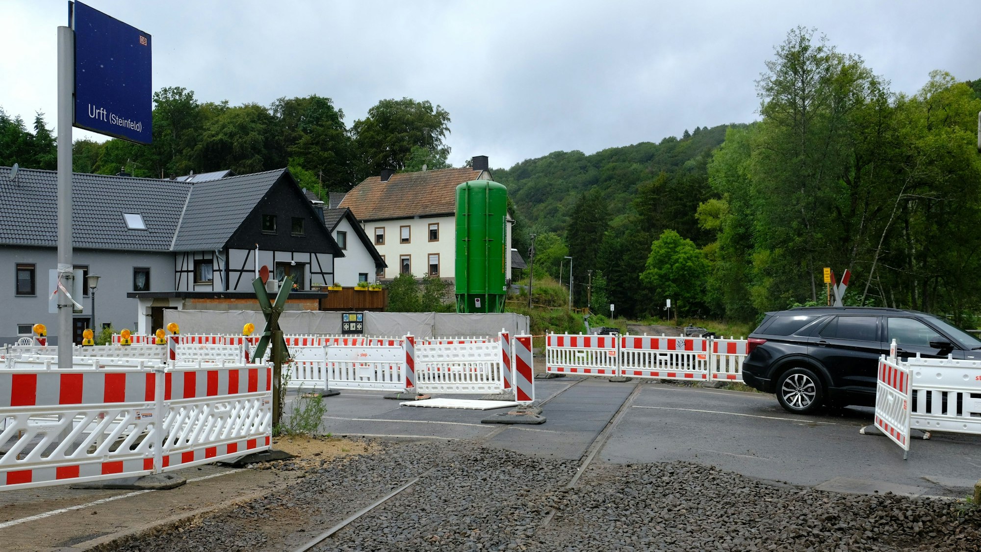 An der Baustelle des Bahnübergangs in Urft stehen Absperrungen, ein Auto fährt vorüber.