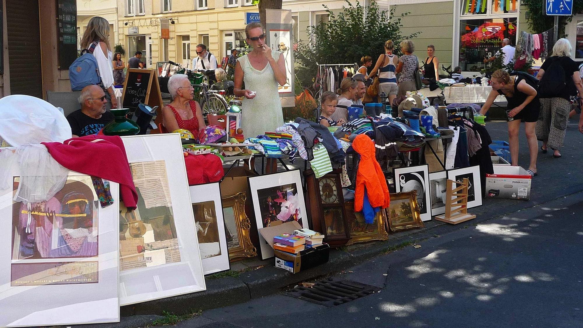 Trödelmarktstände stehen am Straßenrand. Menschen stöbern in der Ware.