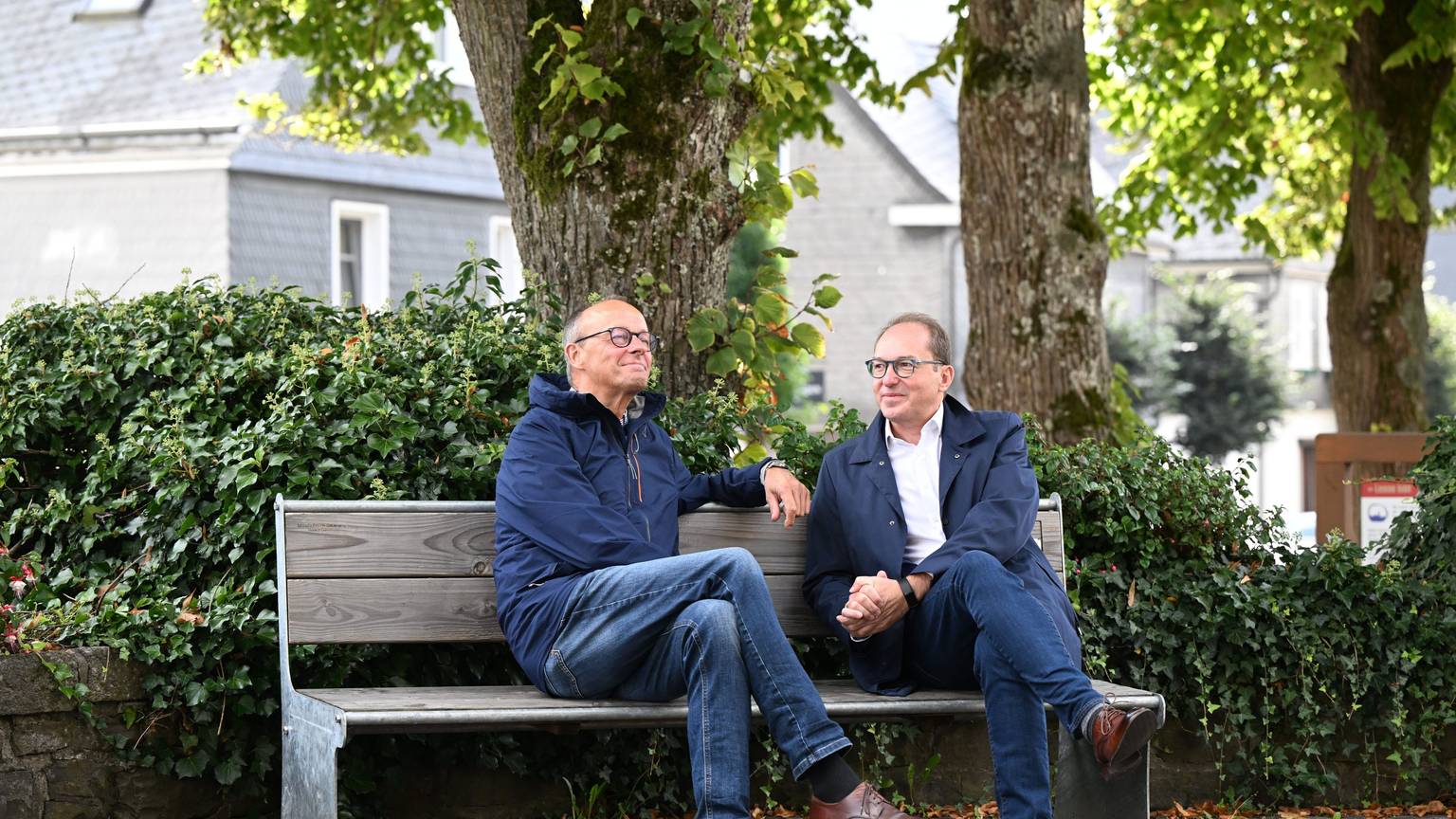 Friedrich Merz und Alexander Dobrindt sitzen gemeinsam auf dem Kirchplatz auf einer Bank.