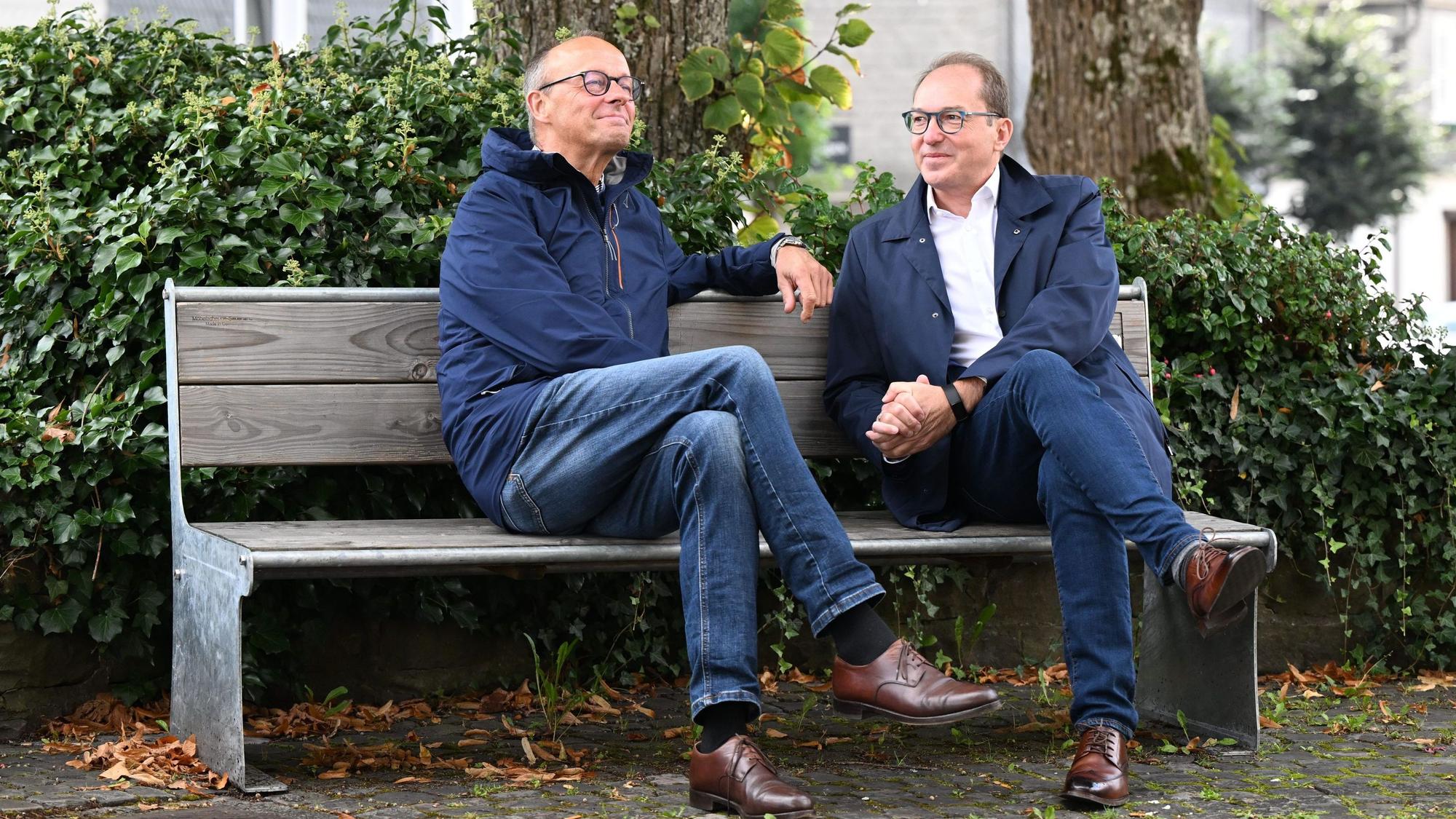 Friedrich Merz und Alexander Dobrindt sitzen gemeinsam auf dem Kirchplatz auf einer Bank.