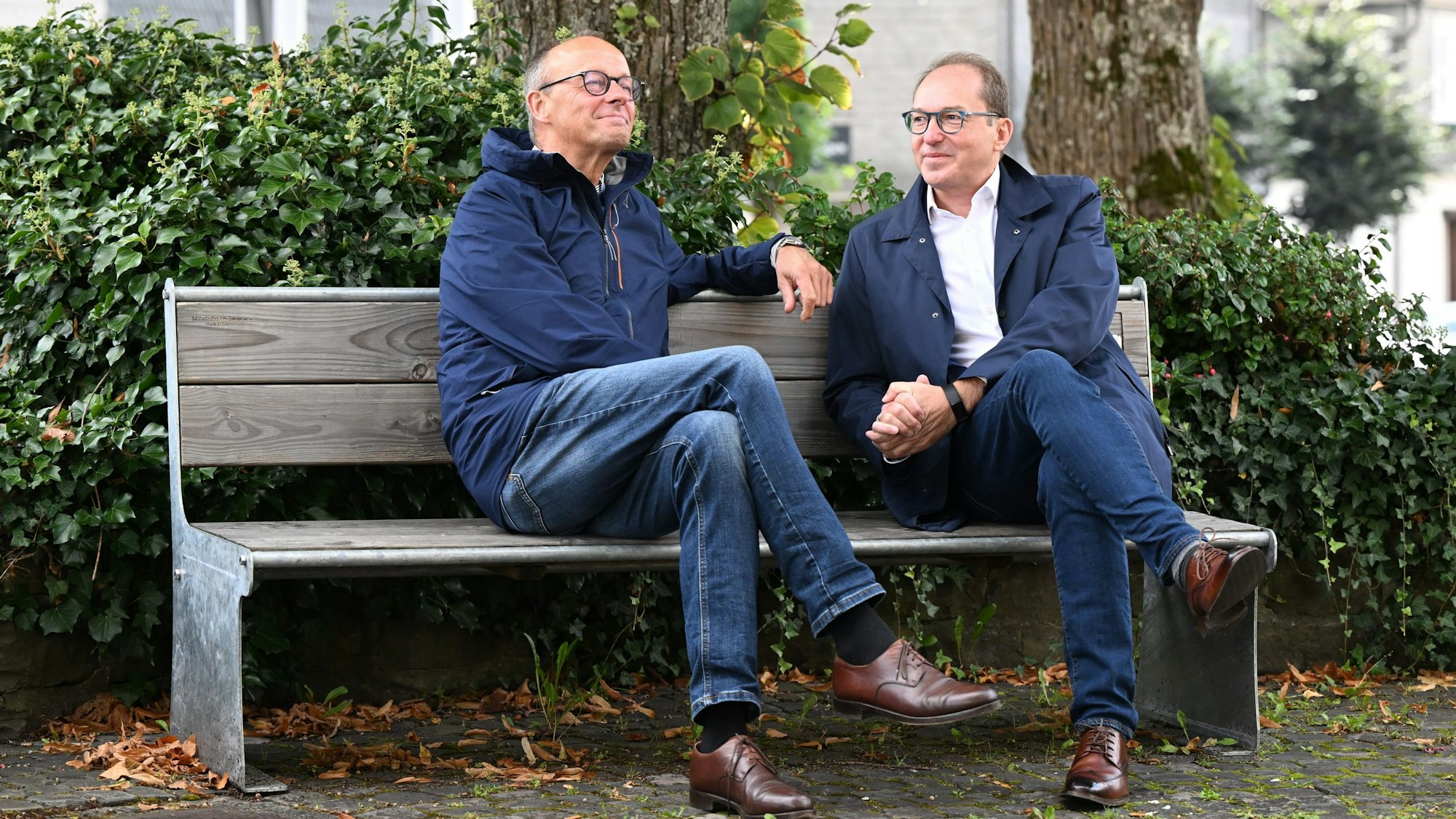 Friedrich Merz und Alexander Dobrindt sitzen gemeinsam auf dem Kirchplatz auf einer Bank.