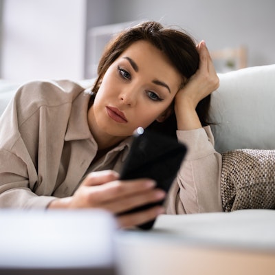 Eine Frau liegt auf der Couch und wartet auf eine Nachricht von der Person, die sie datet.
