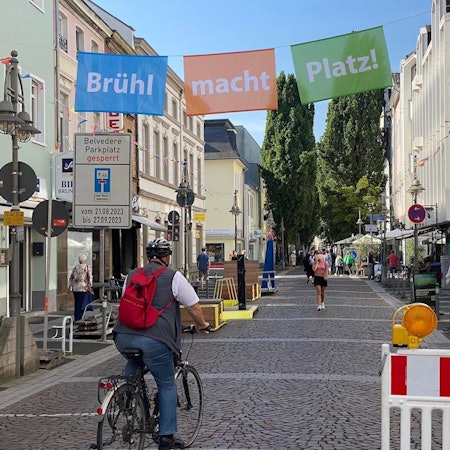 Das Bild zeigt die Kölnstraße, die von einem Banner mit der Aufschrift „Brühl macht Platz“ überspannt ist.