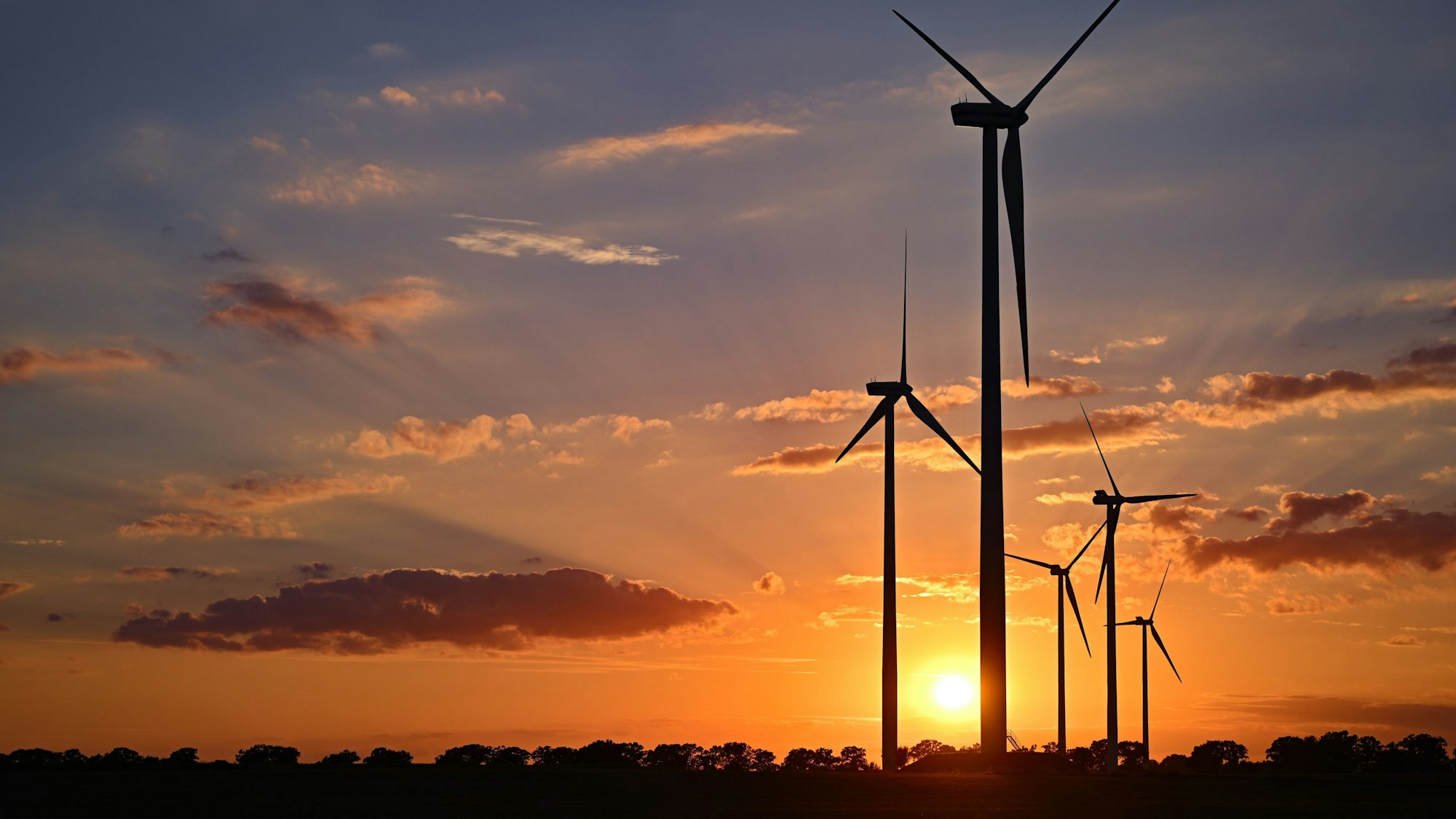 Farbenprächtig leuchtet der Sonnenuntergang über einem Windenergiepark.