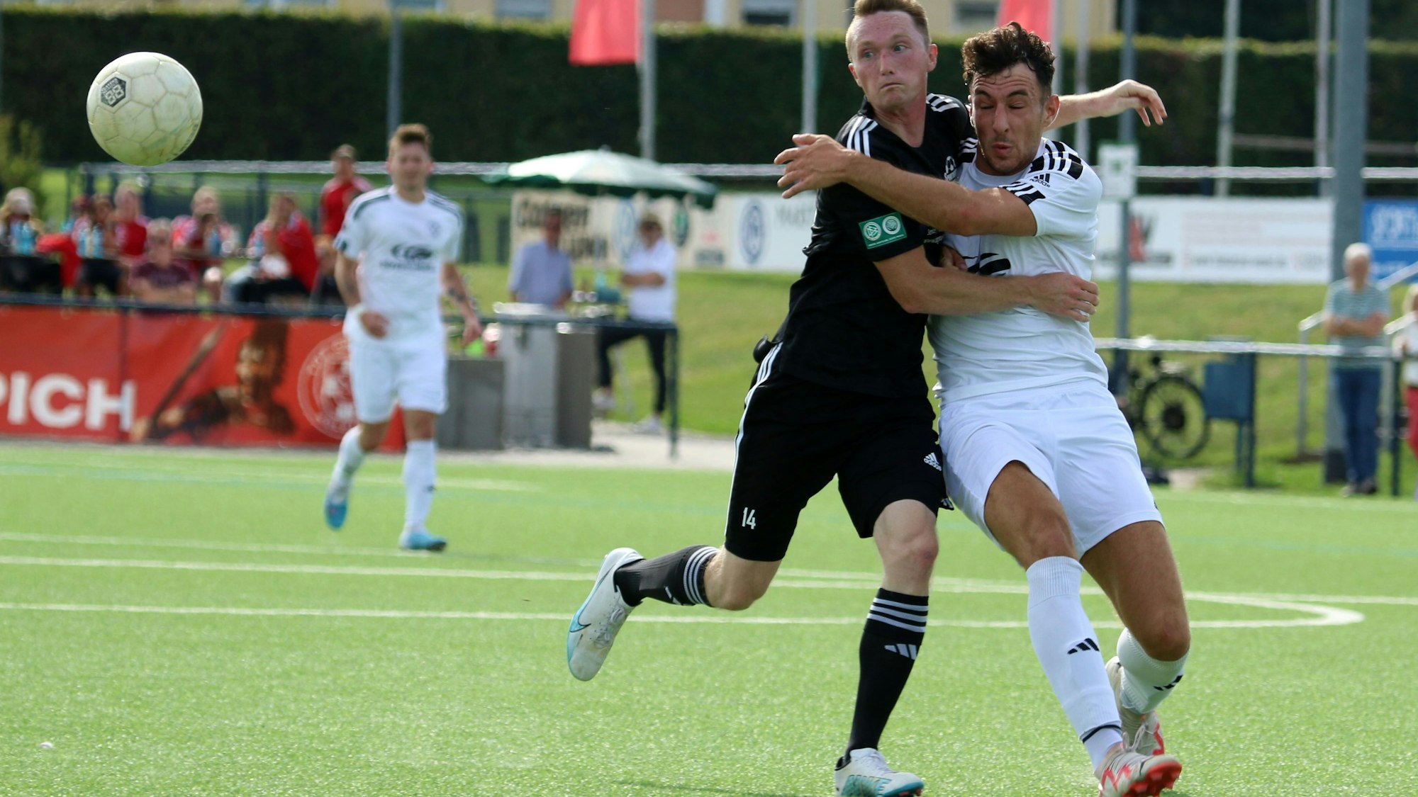 Zwei Fußballer im Zweikampf, beiden haben den Ball, der etwas abseits durch die Luft fliegt, im Blick.