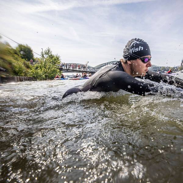 Ein Triathlet beim Schwimmen im Rhein, er trägt einen Neoprenanzug, eine Badekappe und eine Schwimmbrille. Der Kölner Dom und die Hohenzollernbrücke im Hintergrund.