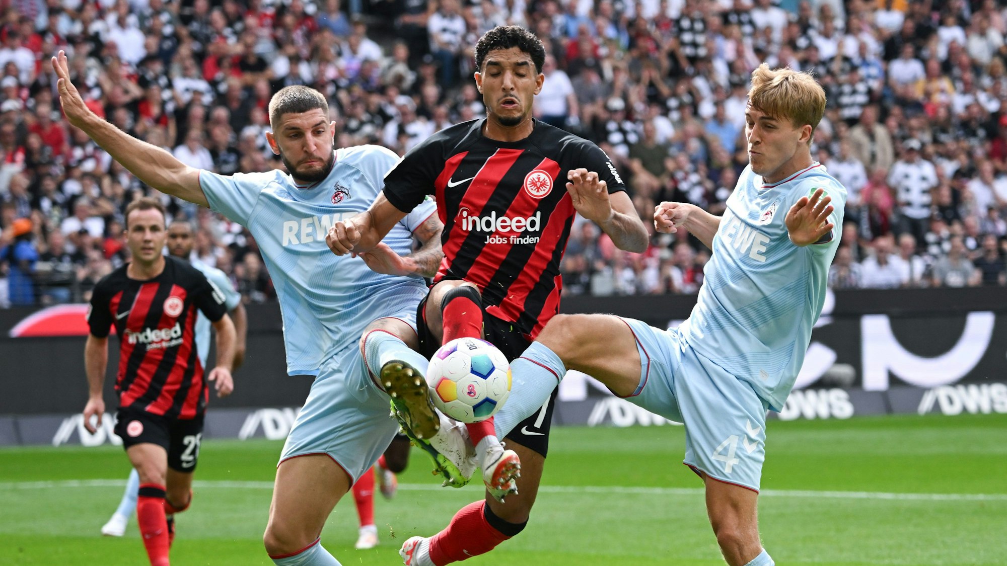 Frankfurts Omar Marmoush (M) und die Kölner Jeff Chabot (l) und Timo Hübers kämpfen um den Ball.