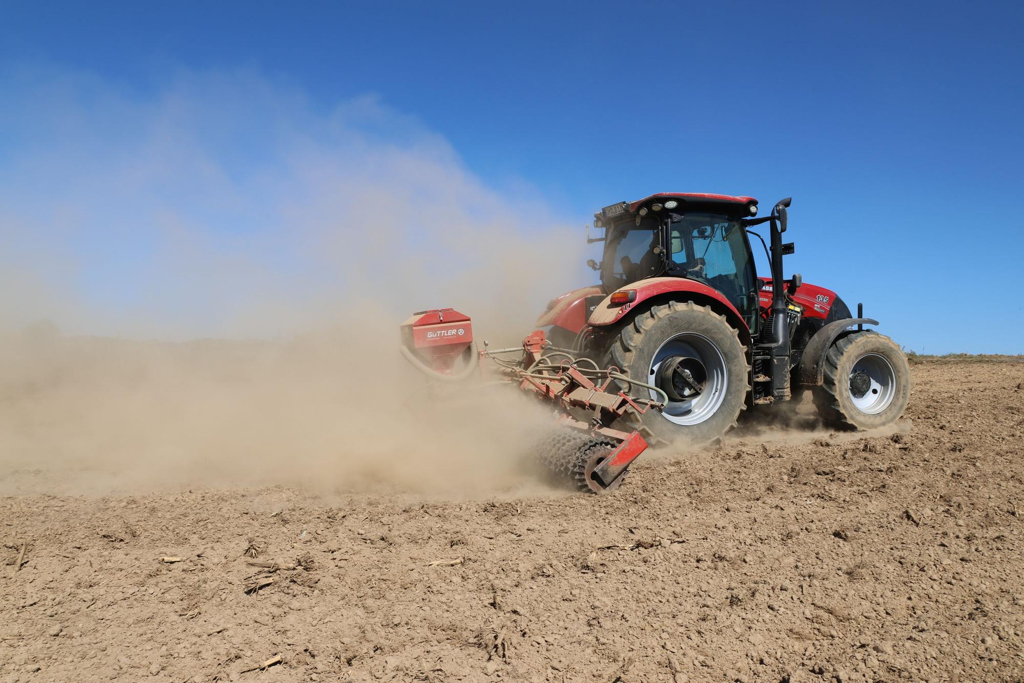 Ein Traktor zieht eine Egge über einen staubigen Acker.