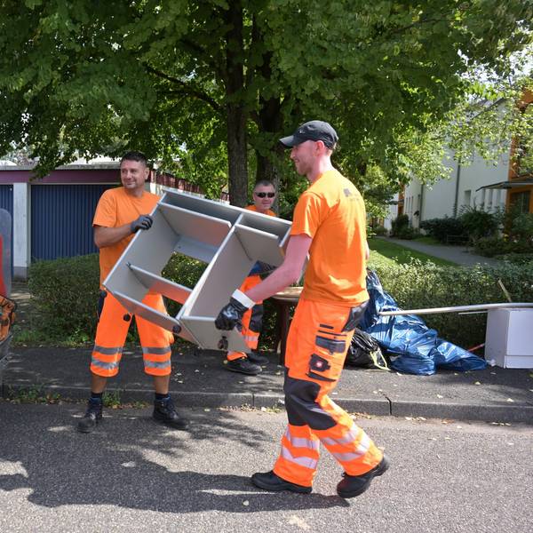 Zwei Männer werfen Sperrmüll in ein Müllfahrzeug.