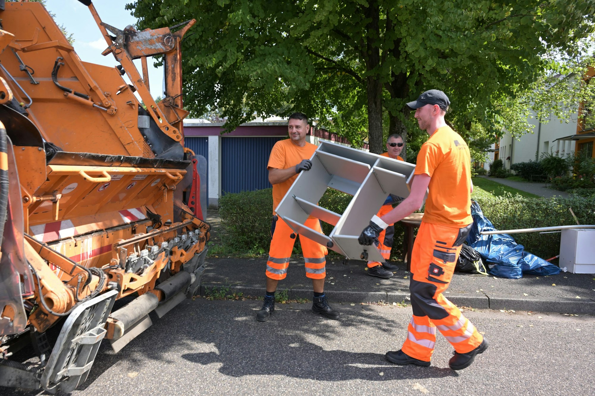 Zwei Männer werfen Sperrmüll in ein Müllfahrzeug.
